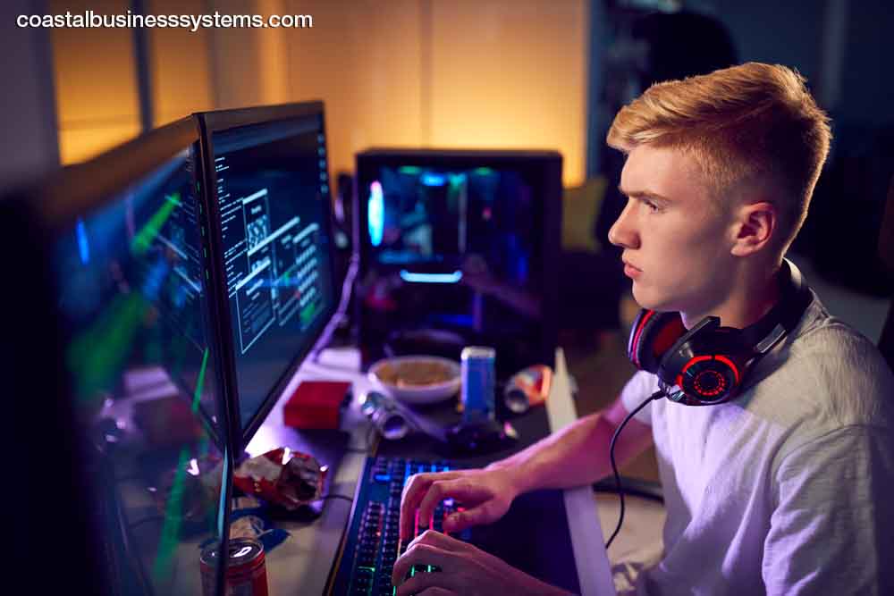 Male Teenage Hacker Sitting In Front Of Computer Screens Bypassing Cyber Security